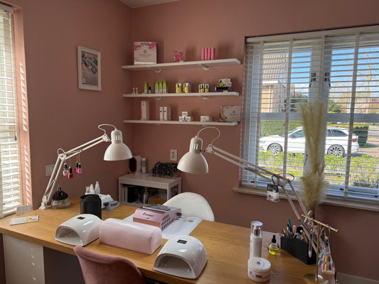 De thuisstudio: een manicuretafel met lamp, handdoeken en gereedschap tegen een warme dusty-rose muur